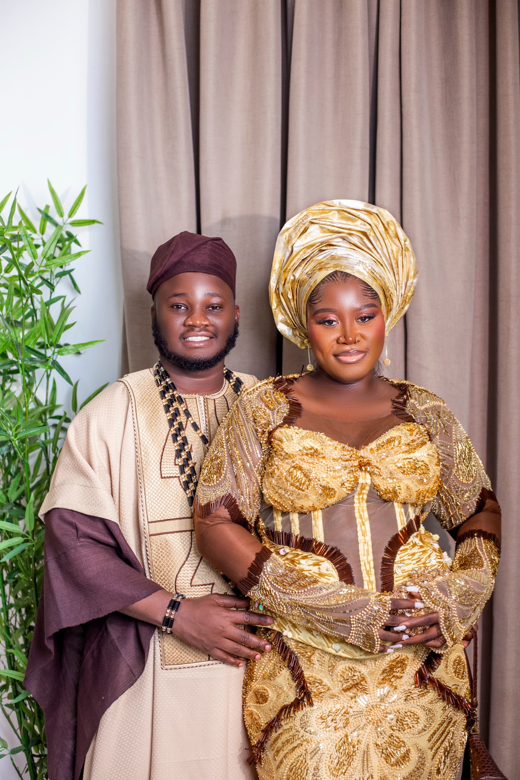 Couple in coordinated gold and wine traditional attire, the bride in a gold gele